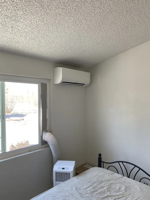 A white wall-mounted ductless mini-split indoor head installed above a window in a bedroom.
