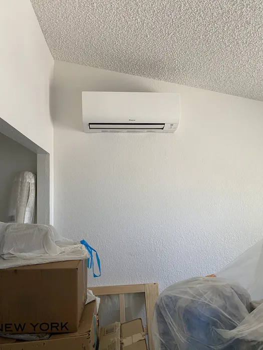 A white wall-mounted ductless mini-split indoor head high in a room corner during a remodel with moving boxes below.