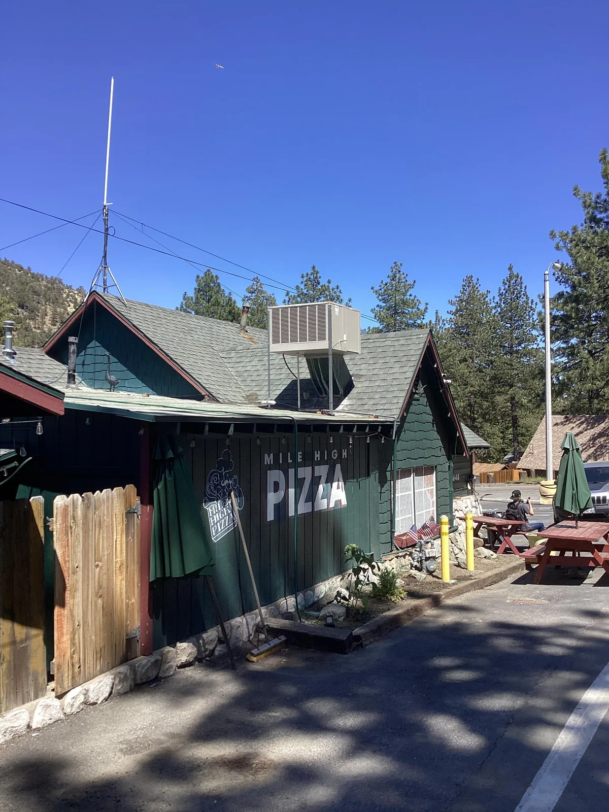 Rooftop-mounted evaporative swamp cooler on the green roof of Mile High Pizza restaurant surrounded by pines under a clear mountain sky.