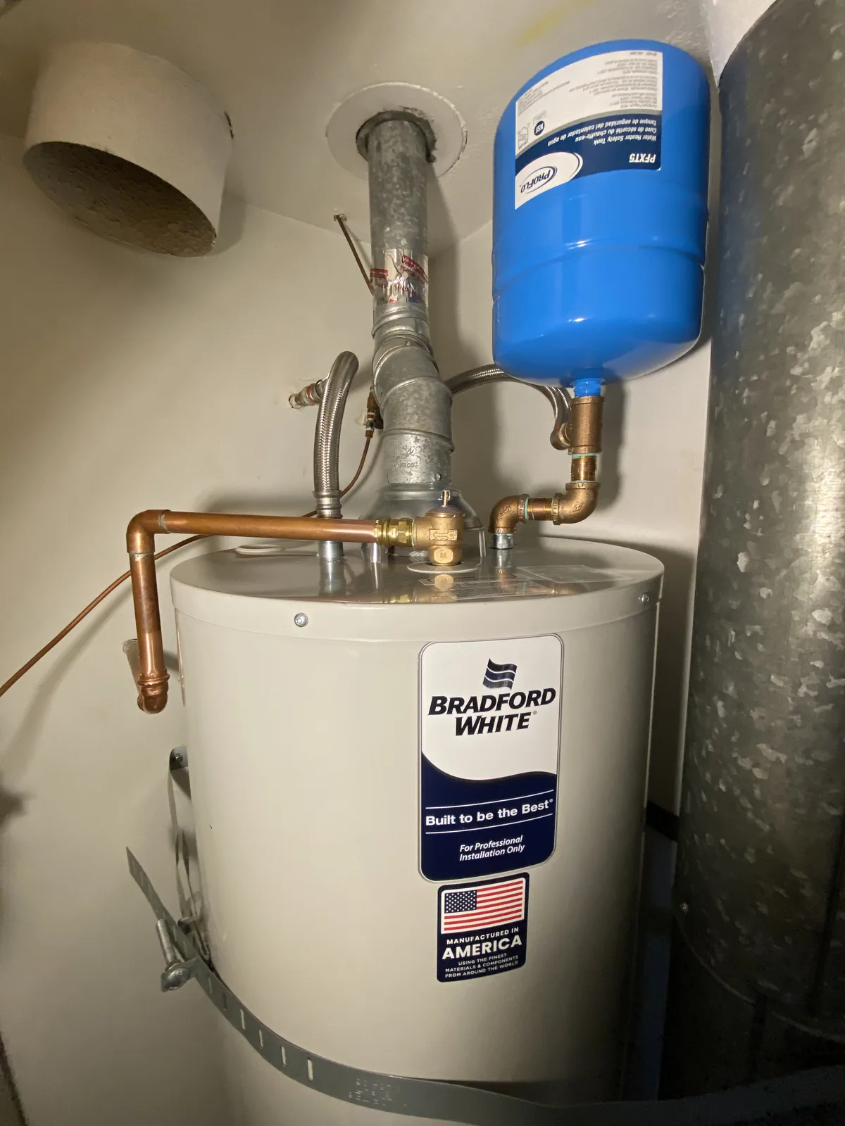 A Bradford White water heater with a blue thermal expansion tank, copper supply lines, and gas control valve installed in a garage.